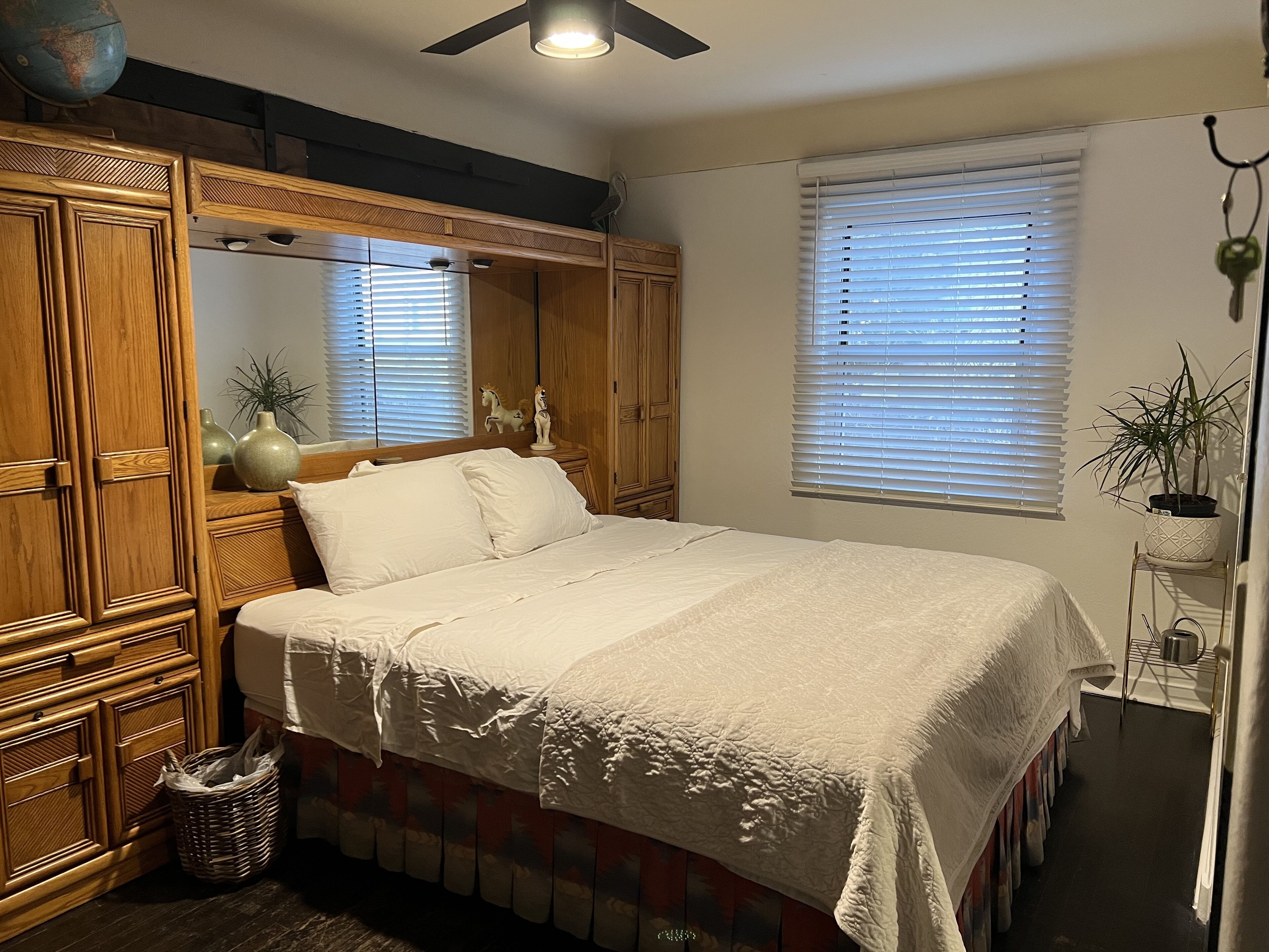Een slaapkamer met een bed, een houten garderobe en een raam met zonwering.