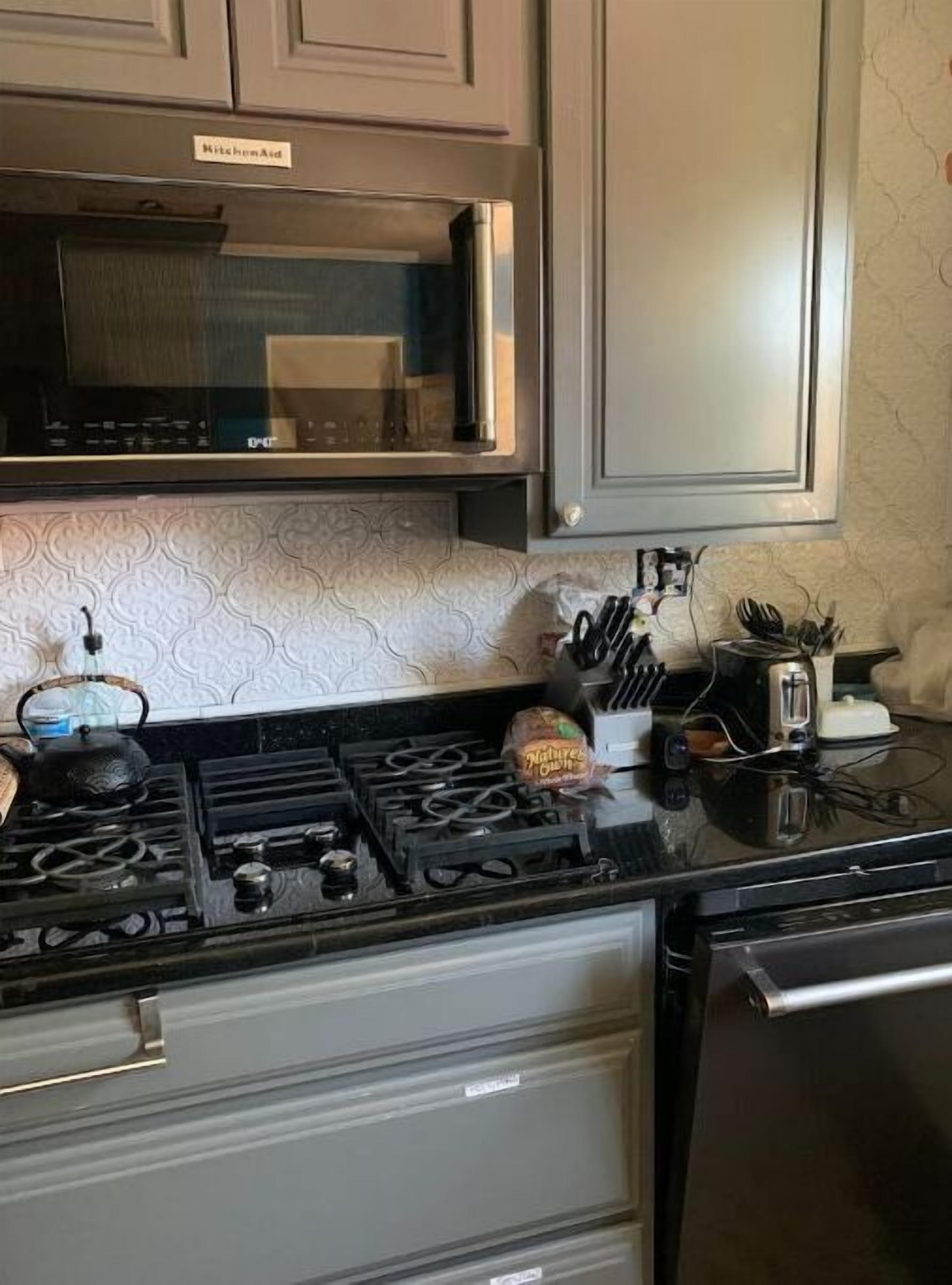 A kitchen with a gas stove, a kettle, a bag of chips, and various utensils on the counter.