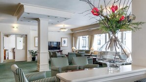 Un vestíbulo de hotel con asientos tapizados a rayas, un jarrón grande con flores rojas y un televisor al fondo.