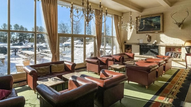 Una habitación acogedora con sofás de cuero, chimenea y grandes ventanales con vistas a un paisaje nevado.