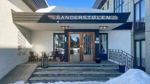La entrada a un edificio llamado 'Sanderstolen', con una puerta de madera, escalones que llevan a ella y un letrero sobre la puerta.