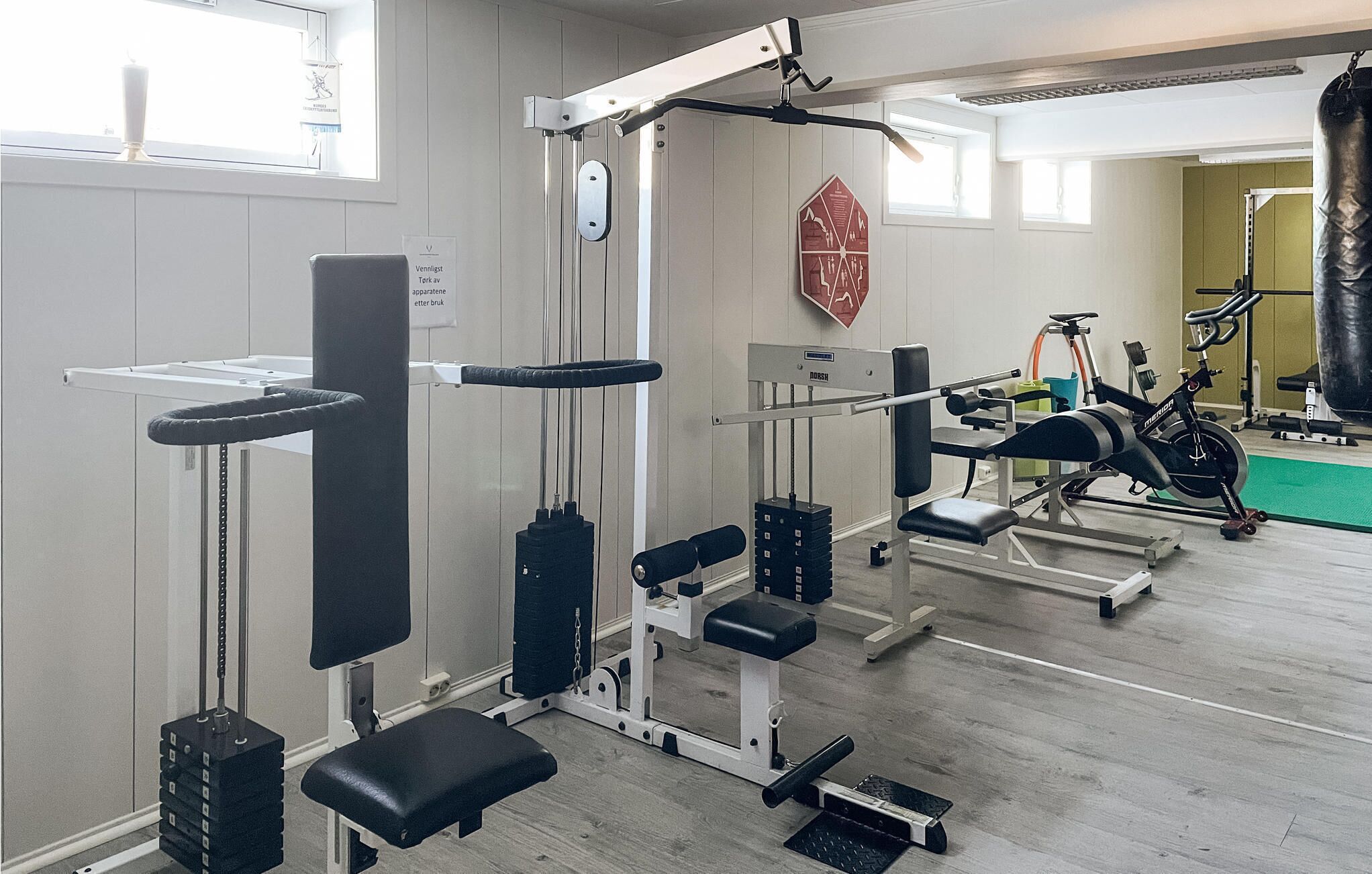 Ein Fitnessstudio mit unterschiedlichen Trainingsgeräten, darunter eine Hantelbank, ein Squat-Gestell und ein Boxsack.