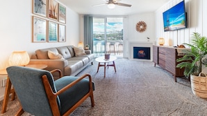 A living room with a sofa, chairs, a fireplace, a TV, and artwork on the wall. - Sunset Harbor and Ocean Views, Modern Coastal Design, Beachfront Resort (Oceanside)