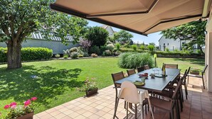 Eine Terrasse im Freien mit Tisch und Stühlen, umgeben von einem gepflegten Rasen und Garten.