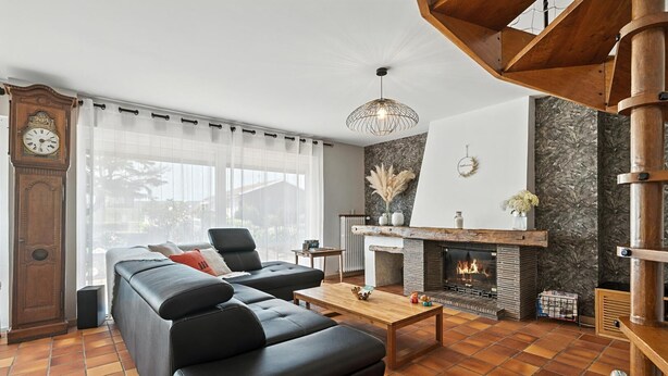 Ein Wohnzimmer mit einer schwarzen Ledersofa, einem Holztisch, einem Kamin und einem großen Fenster mit durchsichtigen Vorhängen.