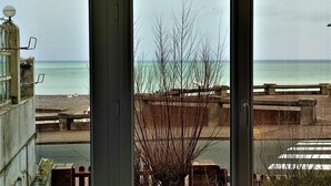Blick auf einen Strand aus einem Fenster mit Meerblick und einer Holzlattenveranda.