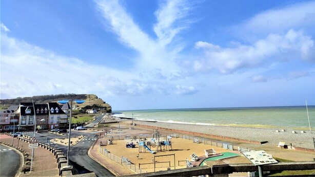 Ein Strand mit einer Promenade, einem Spielplatz und Gebäuden im Hintergrund.