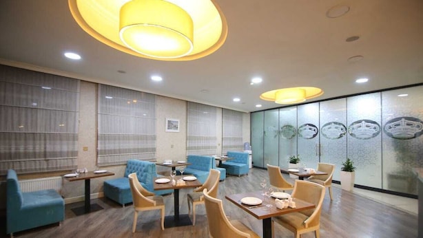 A modern dining area with blue sofas and wooden tables, large windows with blinds, and decorative wall art. - Empire Hotel (Baku)