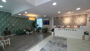 A reception area with a modern design, featuring a reception desk labeled "RECEPTION," a green patterned wall, and a mix of seating arrangements including a sofa and chairs. - Empire Hotel (Baku)
