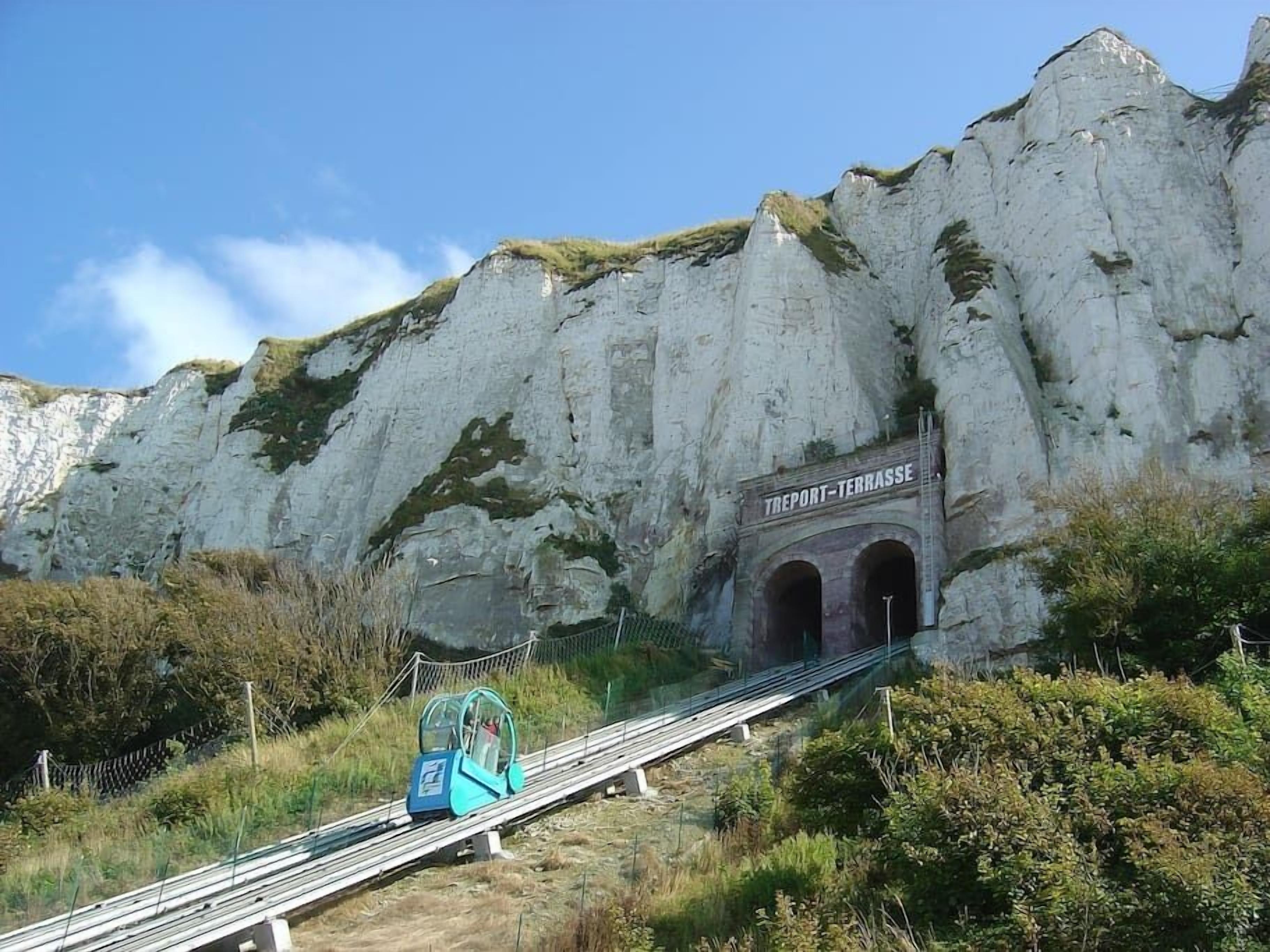 A cable car ascending a steep mountain path towards a rocky cliff with a sign reading "TREPORT-TERRASSE".
