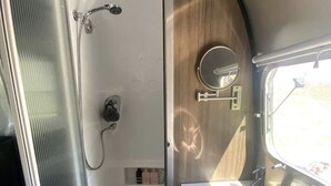 Et kompakt badeværelse i en autocamper med brusebad, vask og et vindue.
