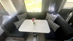 En kompakt autocamper indretning med en sofa, et lille bord og et vindue med udsigt til det fri.