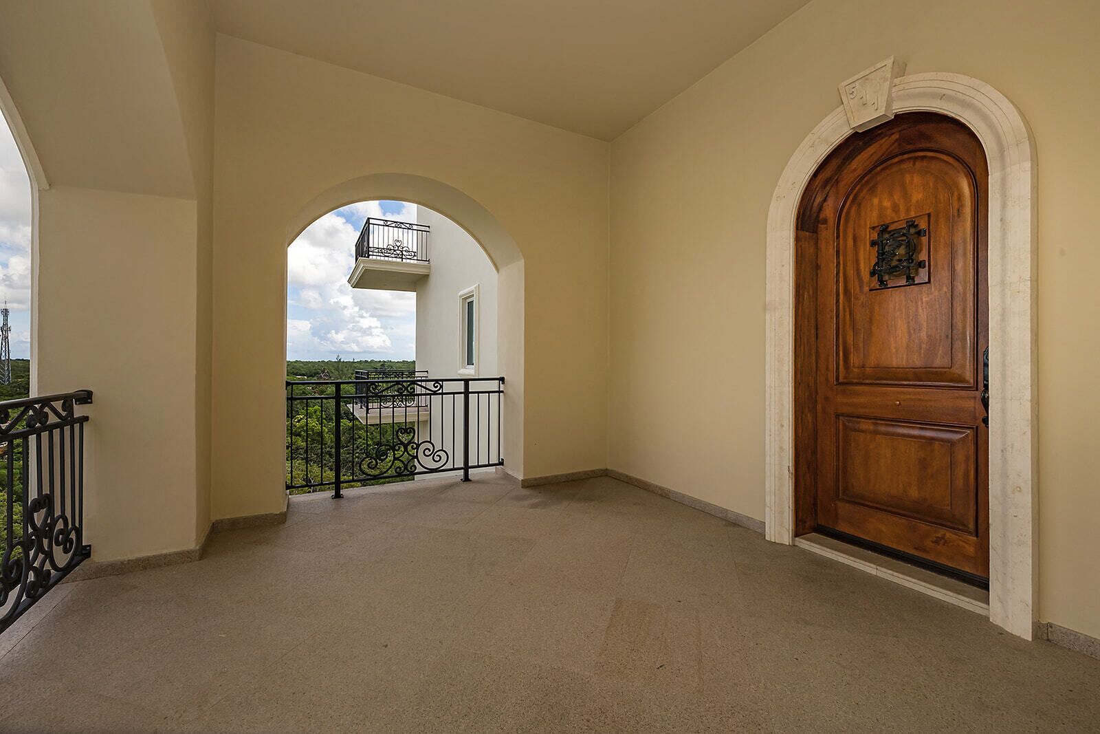 An empty corridor with a wooden door and a balcony with a metal railing.
