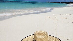 A straw hat on a sandy beach with clear blue water and a distant shoreline. - Luxury Condo Steps from Ocean with Great Views at The Landmark Resort of Cozumel (San Miguel de Cozumel)