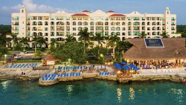 A large hotel with multiple balconies, a beachside bar, and a dock with a boat. - Luxury Condo Steps from Ocean with Great Views at The Landmark Resort of Cozumel (San Miguel de Cozumel)