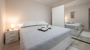 Quarto moderno com uma cama grande, uma mesa de cabeceira com abajur, um espelho e um guarda-roupa.