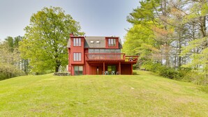 A two-story house with a red exterior, a balcony, and a stone wall in front. - Serene Salisbury Rental Home on 26 Acres w/ Deck! (Salisbury)