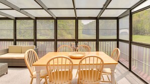 A covered patio with a wooden table and chairs, a cushioned bench, and a view of a forested area. - Serene Salisbury Rental Home on 26 Acres w/ Deck! (Salisbury)