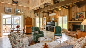 A cozy living room with wooden walls, a fireplace, a piano, and a dining area with a table and chairs. - Serene Salisbury Rental Home on 26 Acres w/ Deck! (Salisbury)