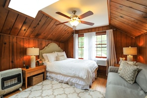 Een gezellige slaapkamer met een houten plafond, een bed met witte beddengoed, een grijze bank en een raam met gordijnen.