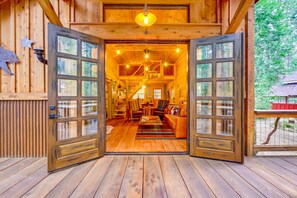 A wooden cabin interior with a large open door, wooden floors, and a cozy living area with furniture.