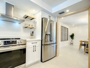 Uma cozinha moderna com eletrodomésticos de aço inoxidável, armários brancos e uma área de refeições com mesa e cadeiras.