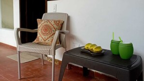 A chair with a patterned cushion, a small table with two green containers and a plate of fruit, and a tiled floor. - San José HOUSE (Leticia)