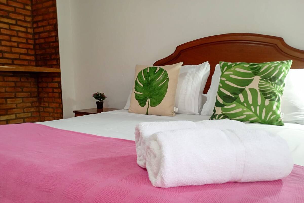 A neatly made bed with a pink bedspread, white pillows, and green leaf-patterned pillows.