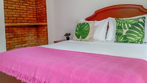 A bedroom with a brick wall, a wooden headboard, a pink bedspread, and tropical-themed pillows. - San José HOUSE (Leticia)