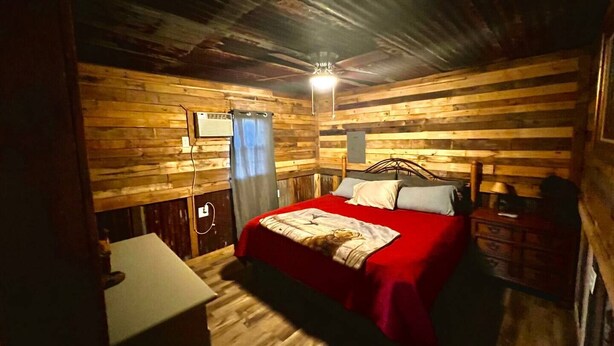 Um quarto acolhedor de madeira, com uma cama, uma mesinha e um ventilador de teto.