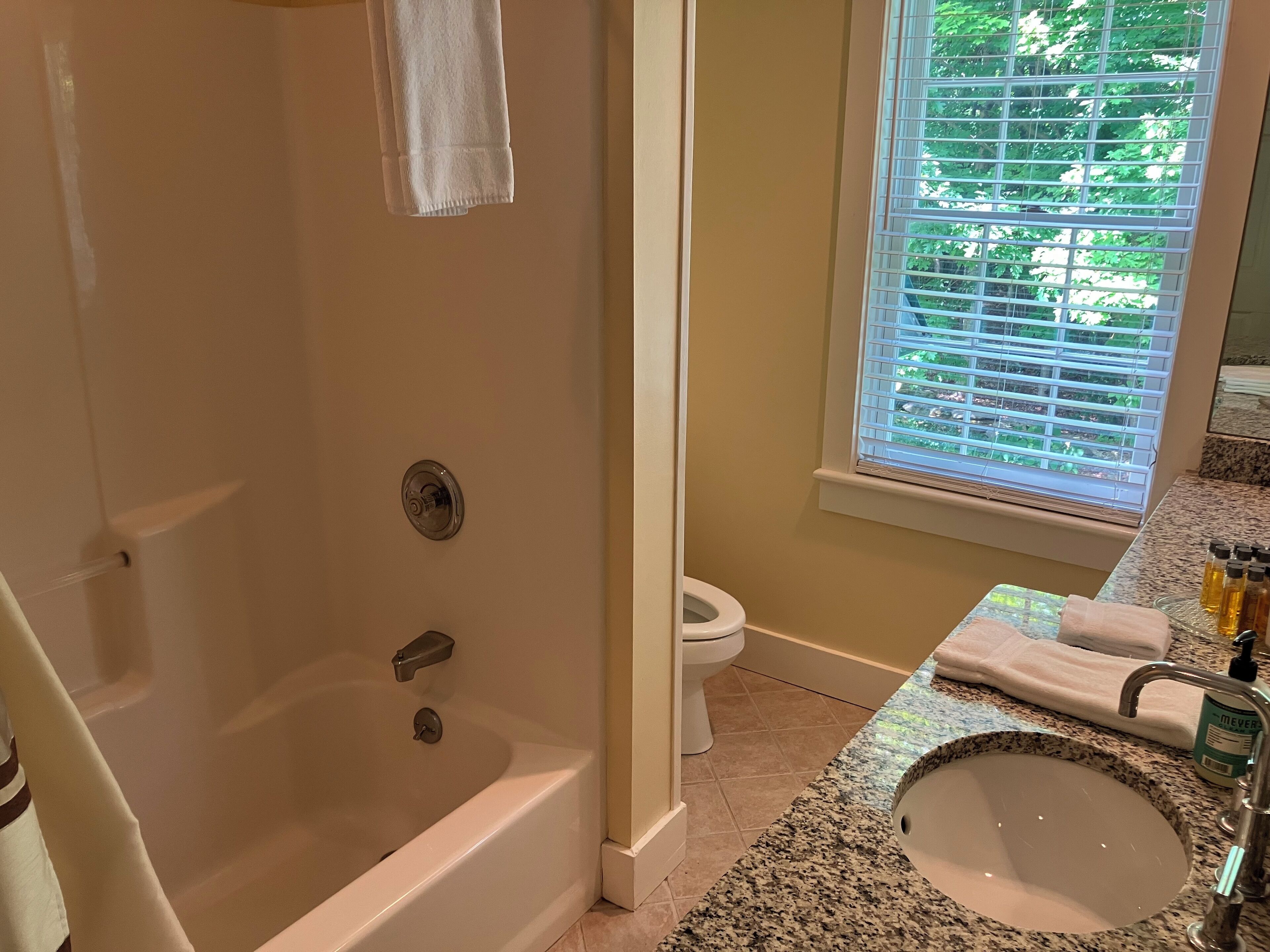 Ein Badezimmer mit Badewanne, Toilette, Waschbecken und einem Fenster mit Jalousien.