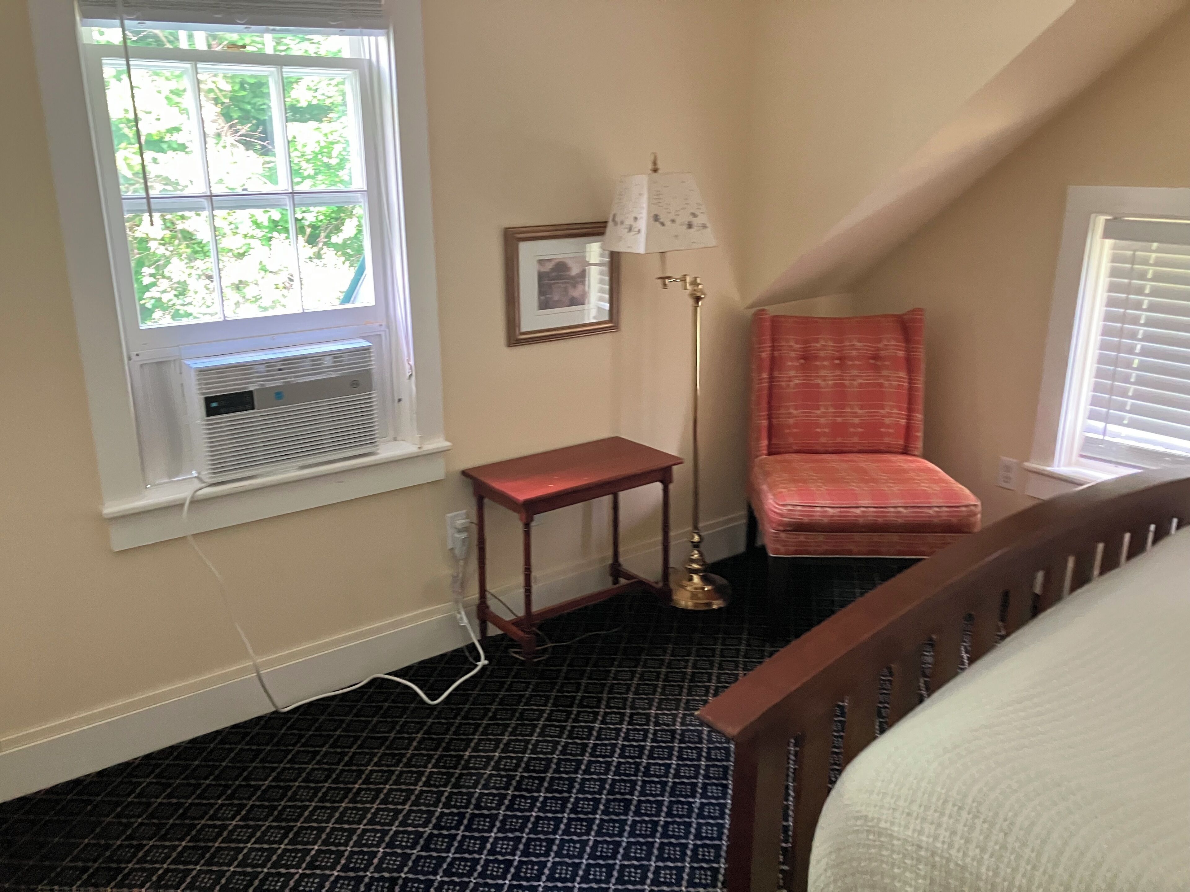 A room with a window, a radiator, a small table, a floor lamp, a patterned chair, and a bed.