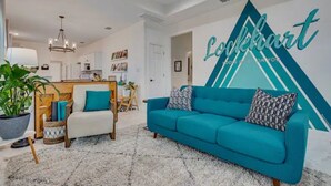 Ein modernes Wohnzimmer mit einem türkisfarbenen Sofa, einem weißen Sessel und einer großen Wandmalerei.