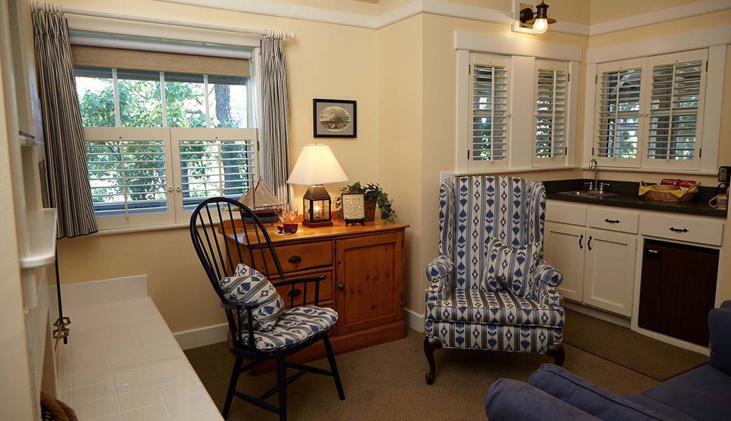 A cozy kitchen with wooden cabinets, a dining area with a chair and table, and a window with curtains.