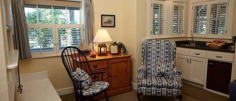 A cozy kitchen with wooden cabinets, a dining area with a chair and table, and a window with curtains.