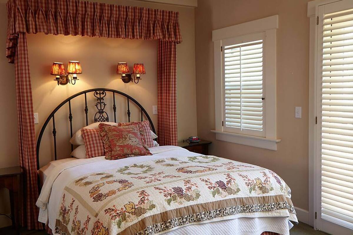 A bedroom with a bed, two wall-mounted lamps, a window with blinds, and a checkered curtain.