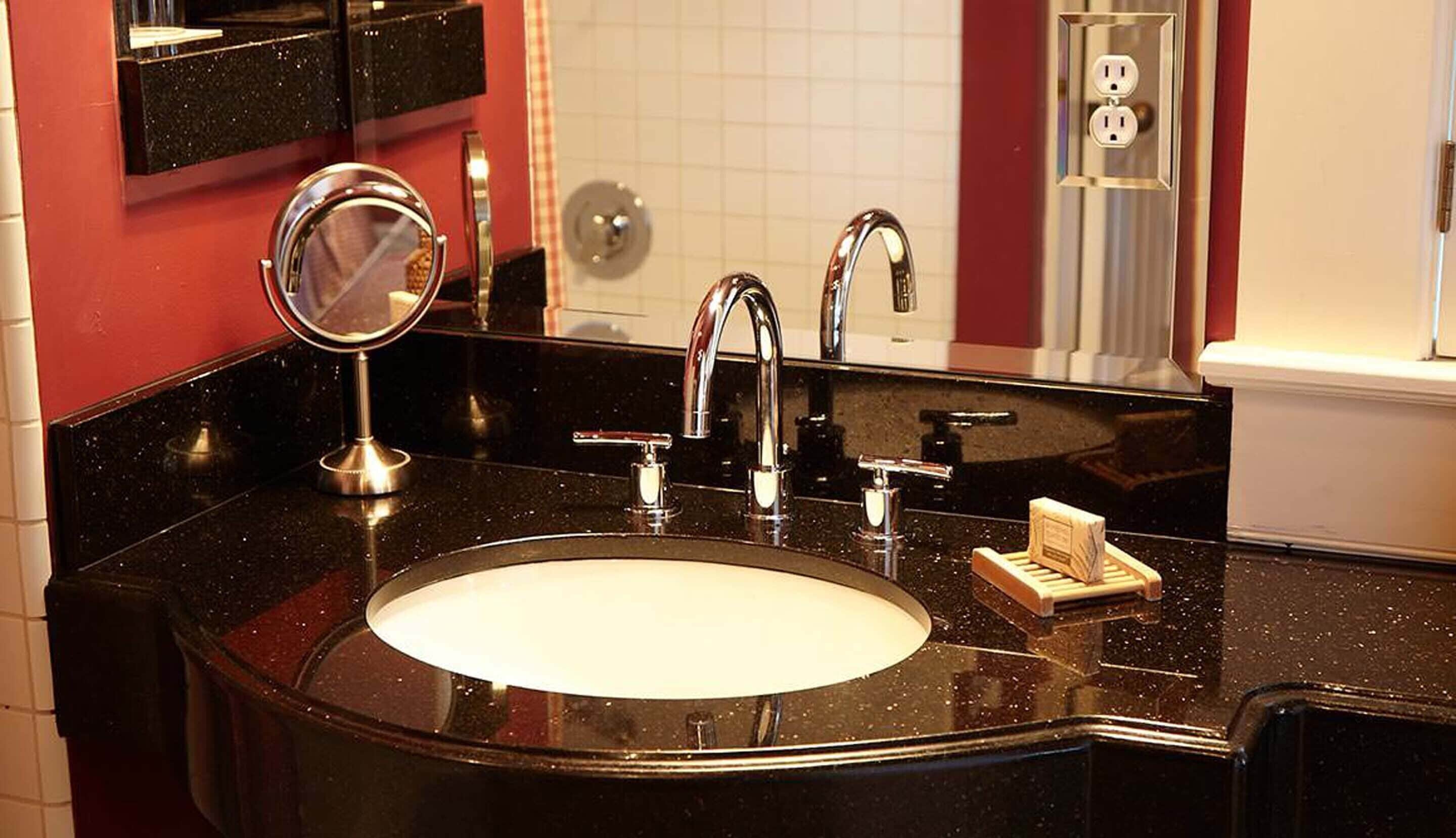 Een badkamer met een zwart aanrecht, een wit wastafel, een spiegel en een zeepbakje.
