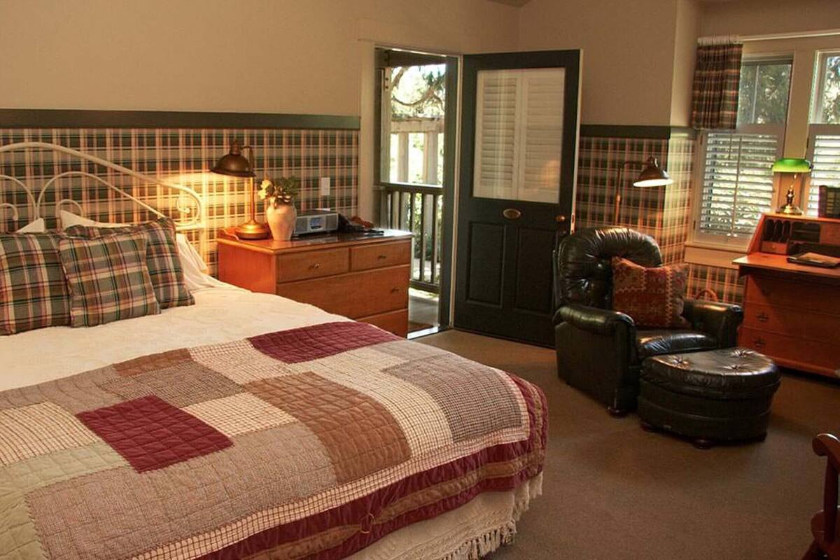 A bedroom with a bed, a nightstand, a chair, a desk, and a door.