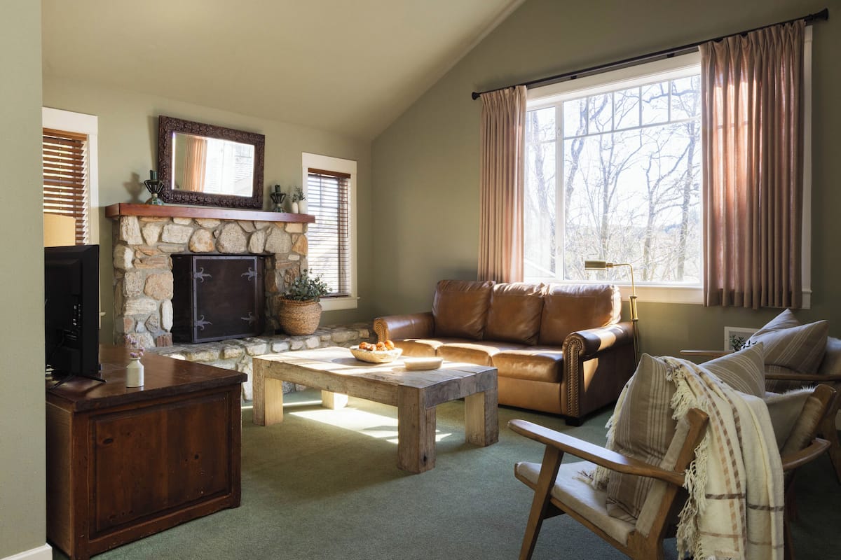 A cozy living room with a stone fireplace, leather sofa, and a wooden coffee table.