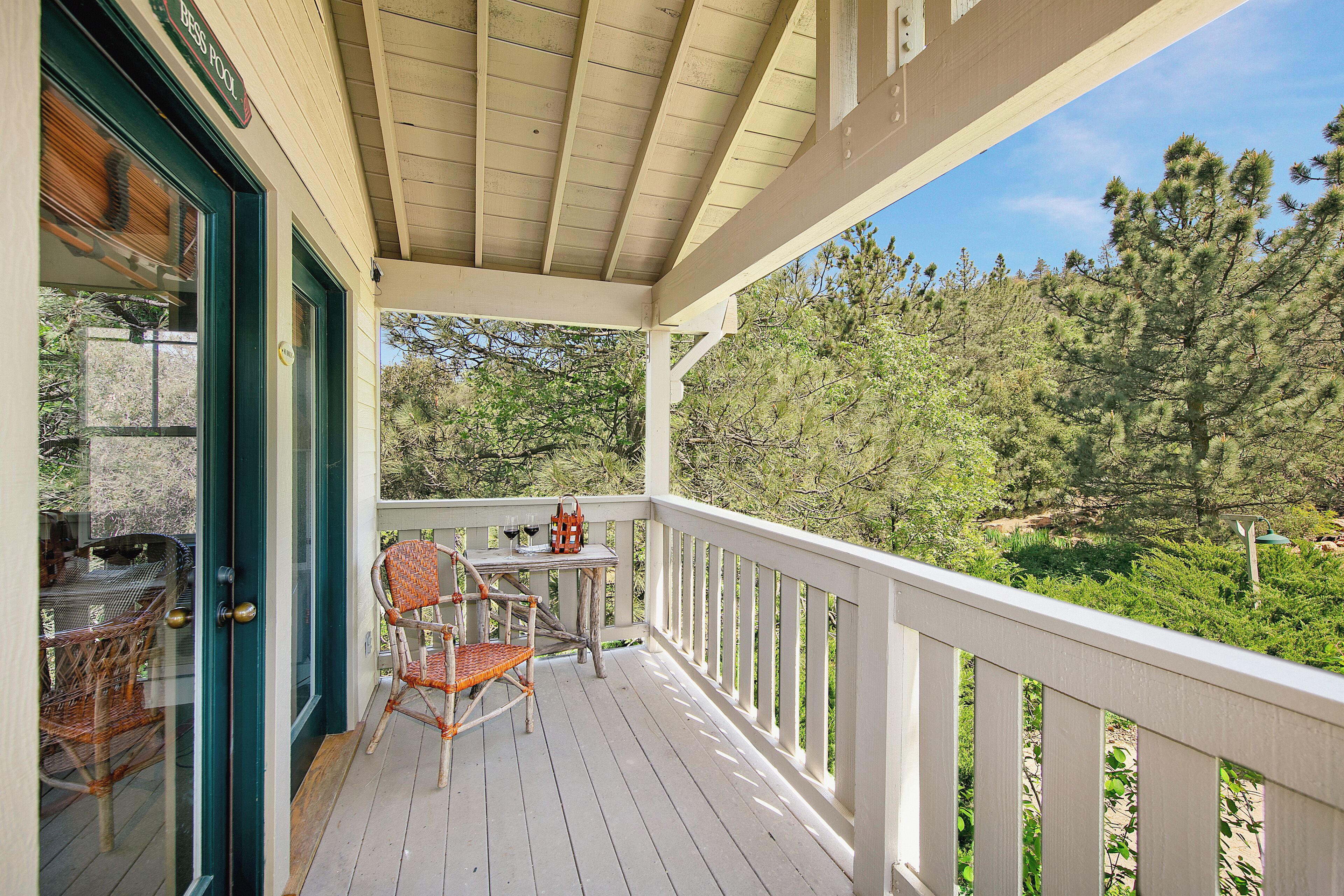 A wooden deck with a table and chairs, a glass door, and a view of trees.