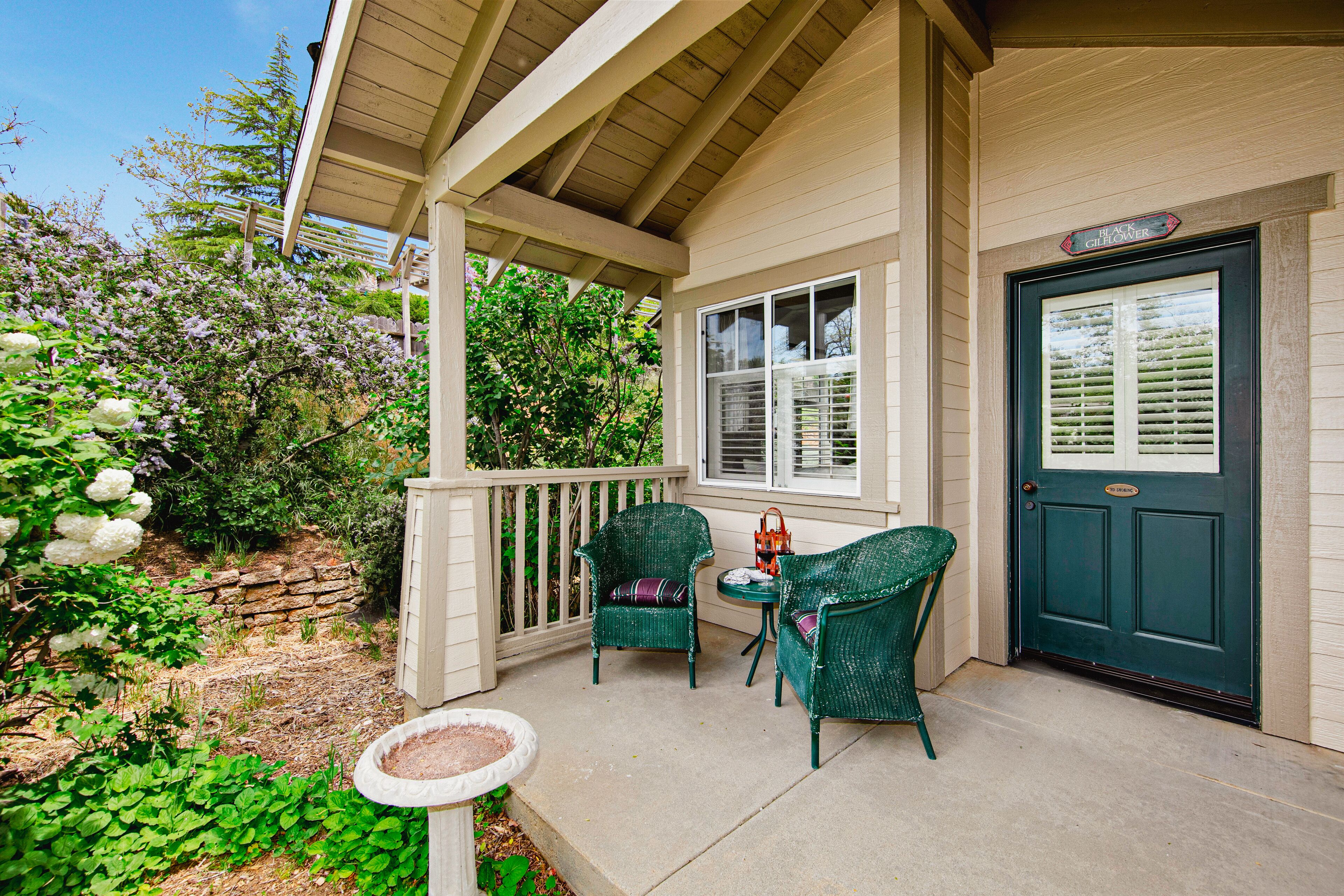 A covered porch with two green wicker chairs, a small table, and a potted plant.