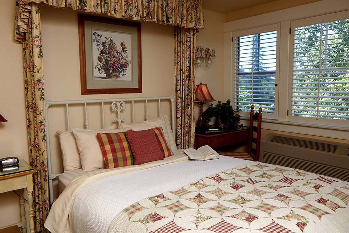 A bedroom with a bed, two bedside tables, a nightstand, a window with blinds, and a framed picture on the wall.