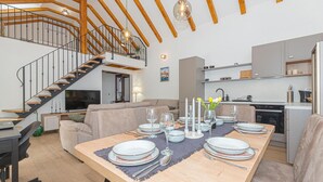 A modern living space with a dining area set for a meal, a kitchen, and a staircase leading to an upper level.