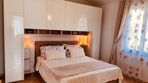 Un dormitorio con cama, lámparas de noche, armario y ventana con cortinas florales.