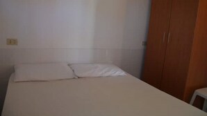 A single bed with white bedding in a room with white walls and a wooden wardrobe.