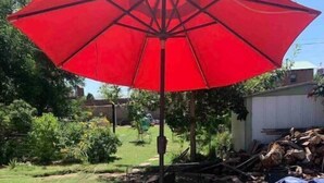Een patio met een rode parasol, een houten stoel en een metalen tafel.
