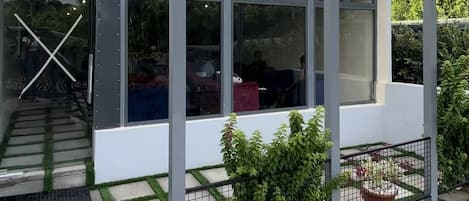 A modern structure with a glass enclosure, labeled "Mango Lounge," featuring a patio area with a stone pathway and potted plants.