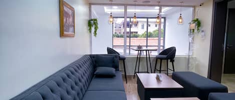 A modern lounge area with a long dark sofa, wooden tables, and hanging pendant lights.