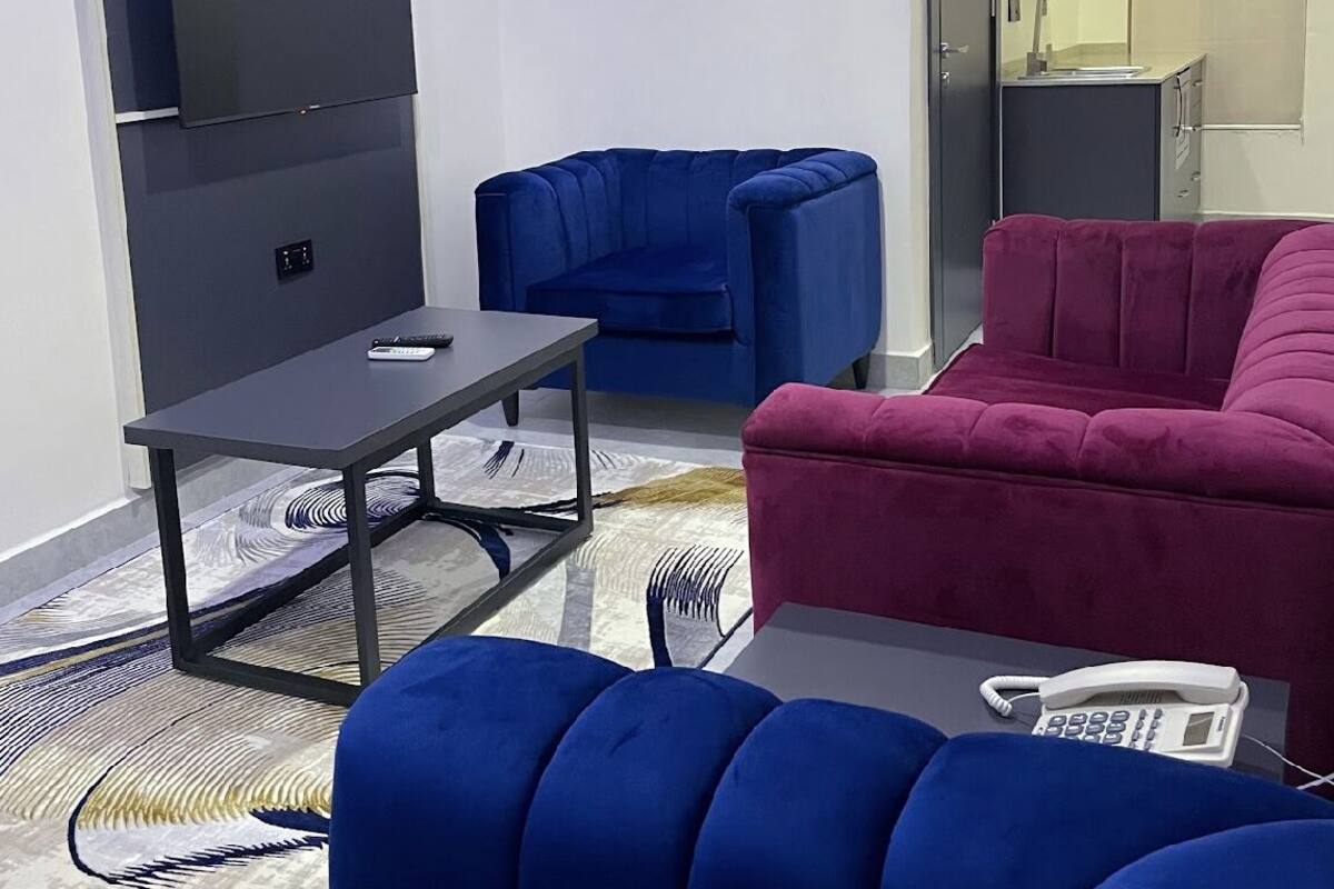 Una sala de estar moderna con un televisor de pantalla plana montado en la pared, un sofá azul, un sofá rojo y una pequeña mesa con un control remoto.