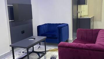 Una sala de estar moderna con un televisor de pantalla plana montado en la pared, un sofá azul, un sofá rojo y una pequeña mesa con un control remoto.